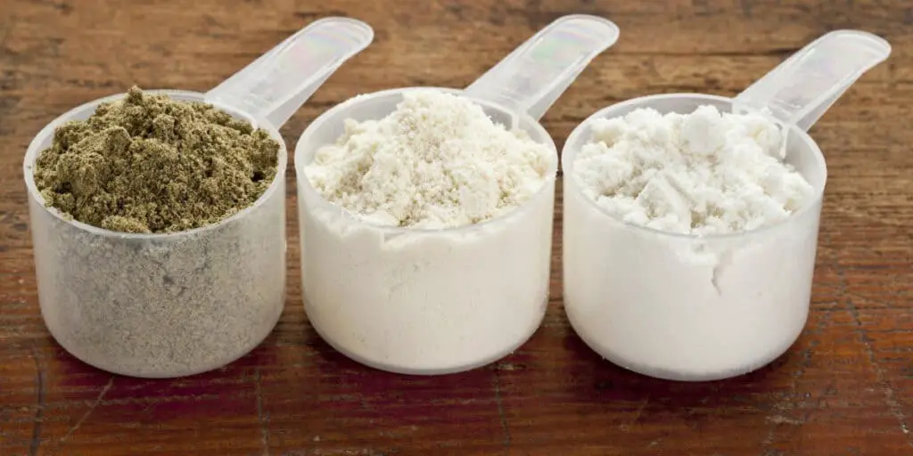 plastic measuring scoops of three protein powders (from left hemp seed, whey concentrate, whey isolate) on a grunge wood surface