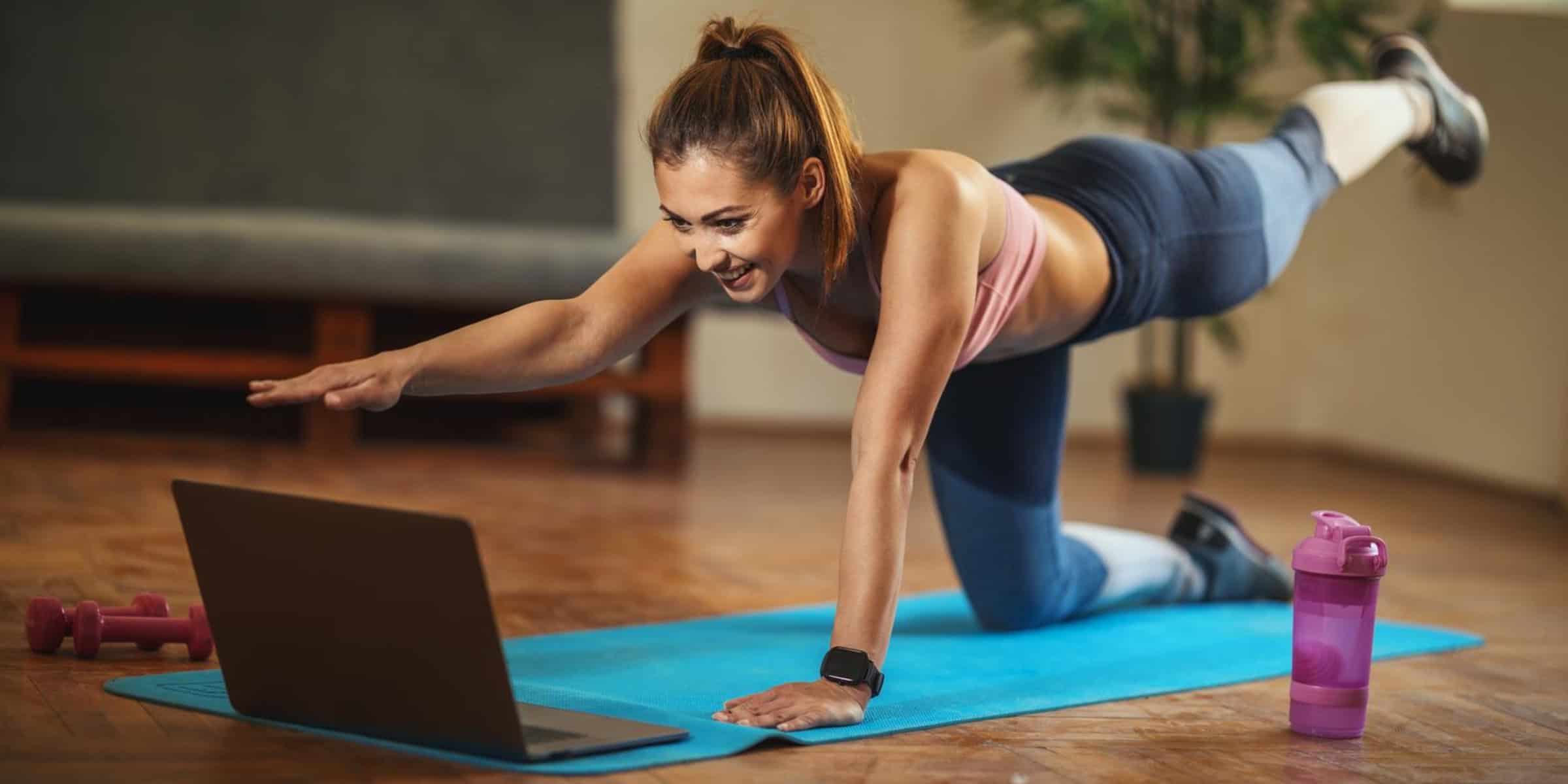 A woman doing yoga on a yoga mat while using a laptop.