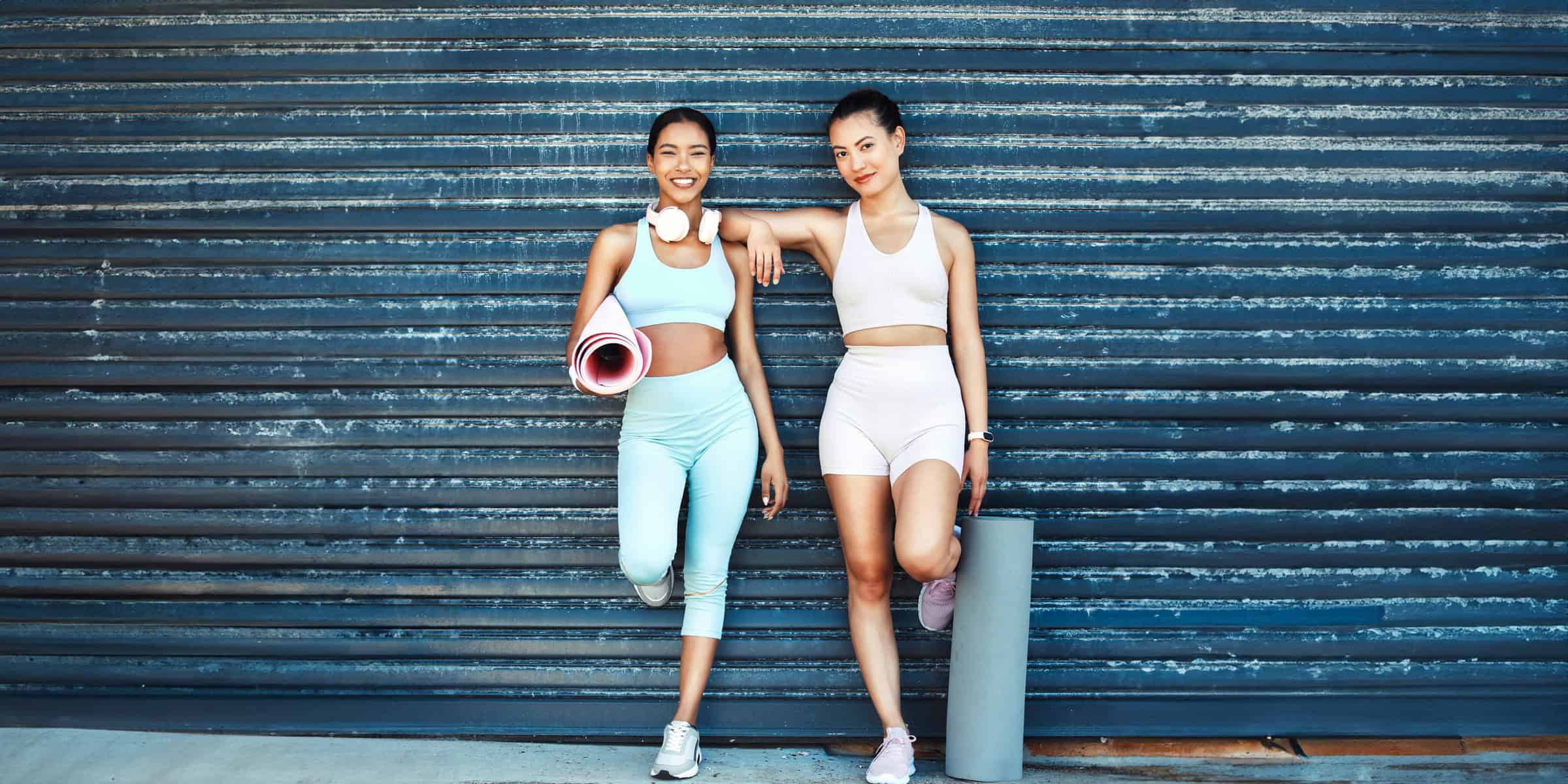 Two asian women standing next to each other holding a yoga mat.