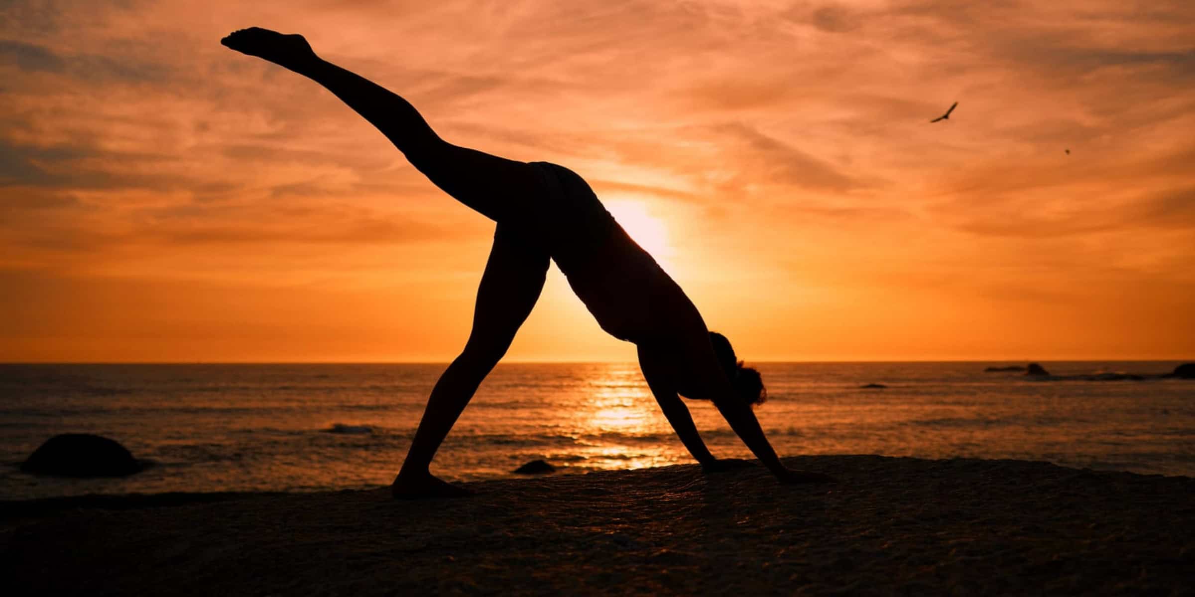 A silhouette of a woman doing Pilates on the beach at sunset.