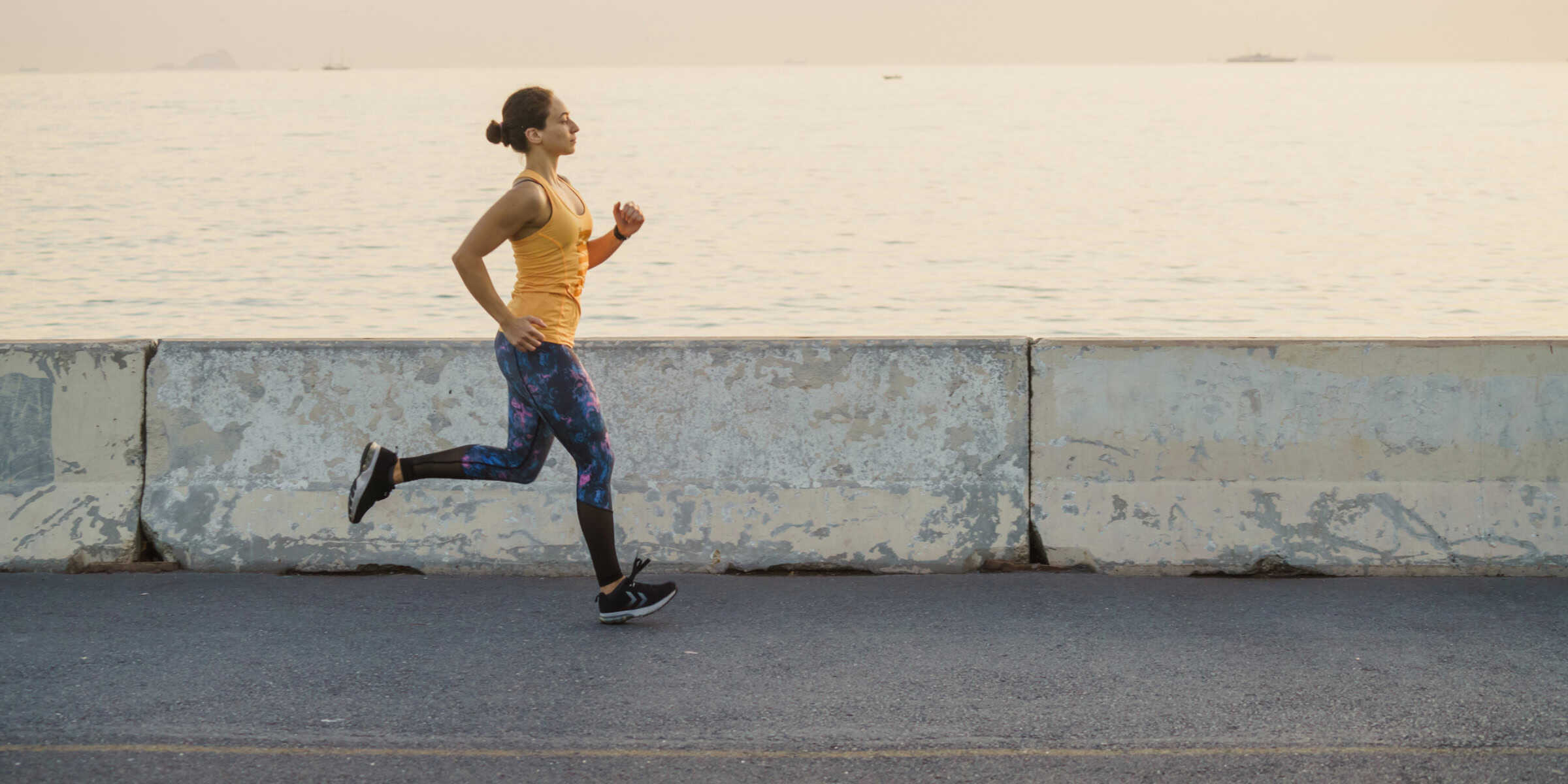 A woman is jogging near the water.