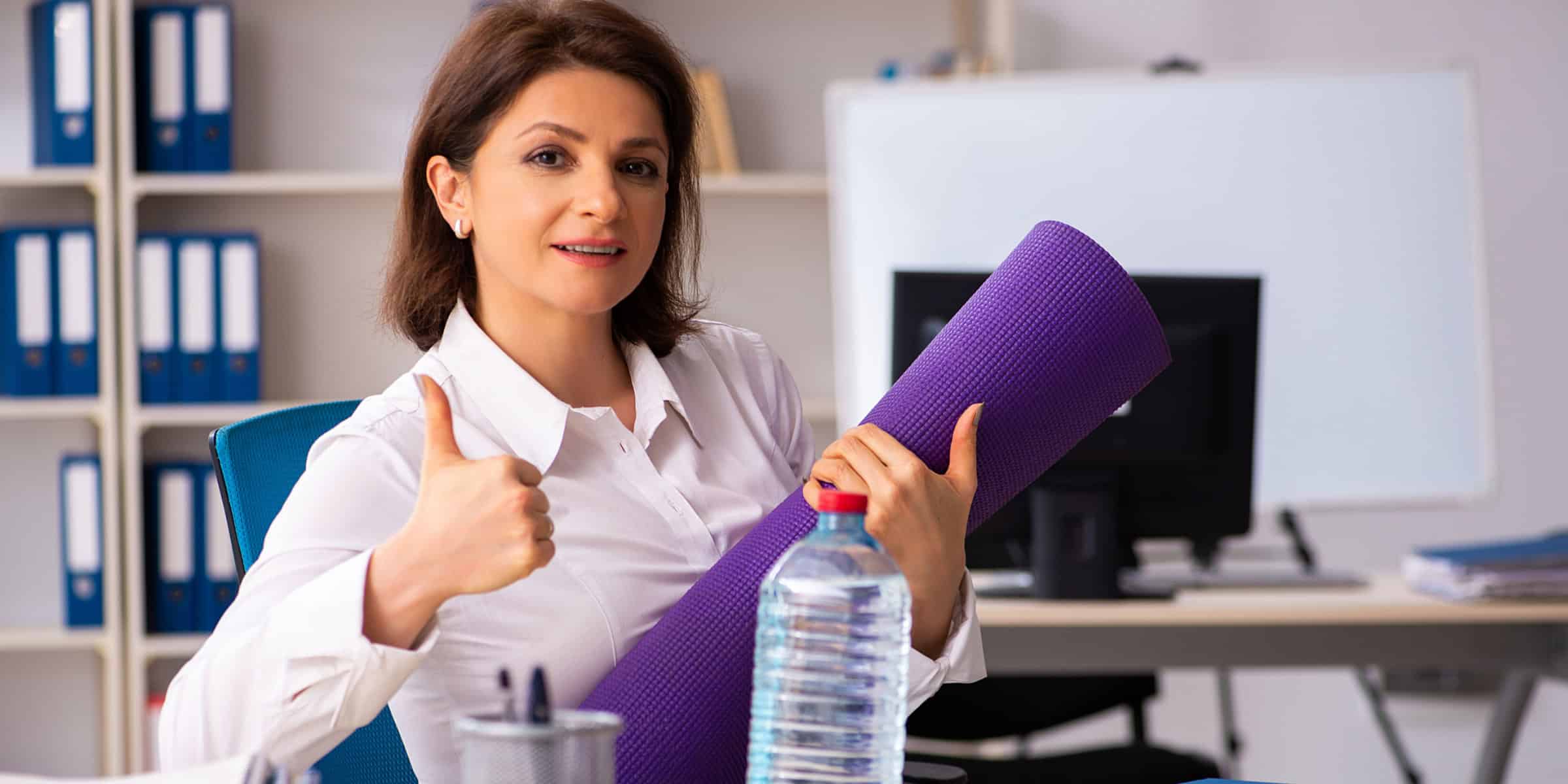 A woman is holding a yoga mat and giving thumbs up.