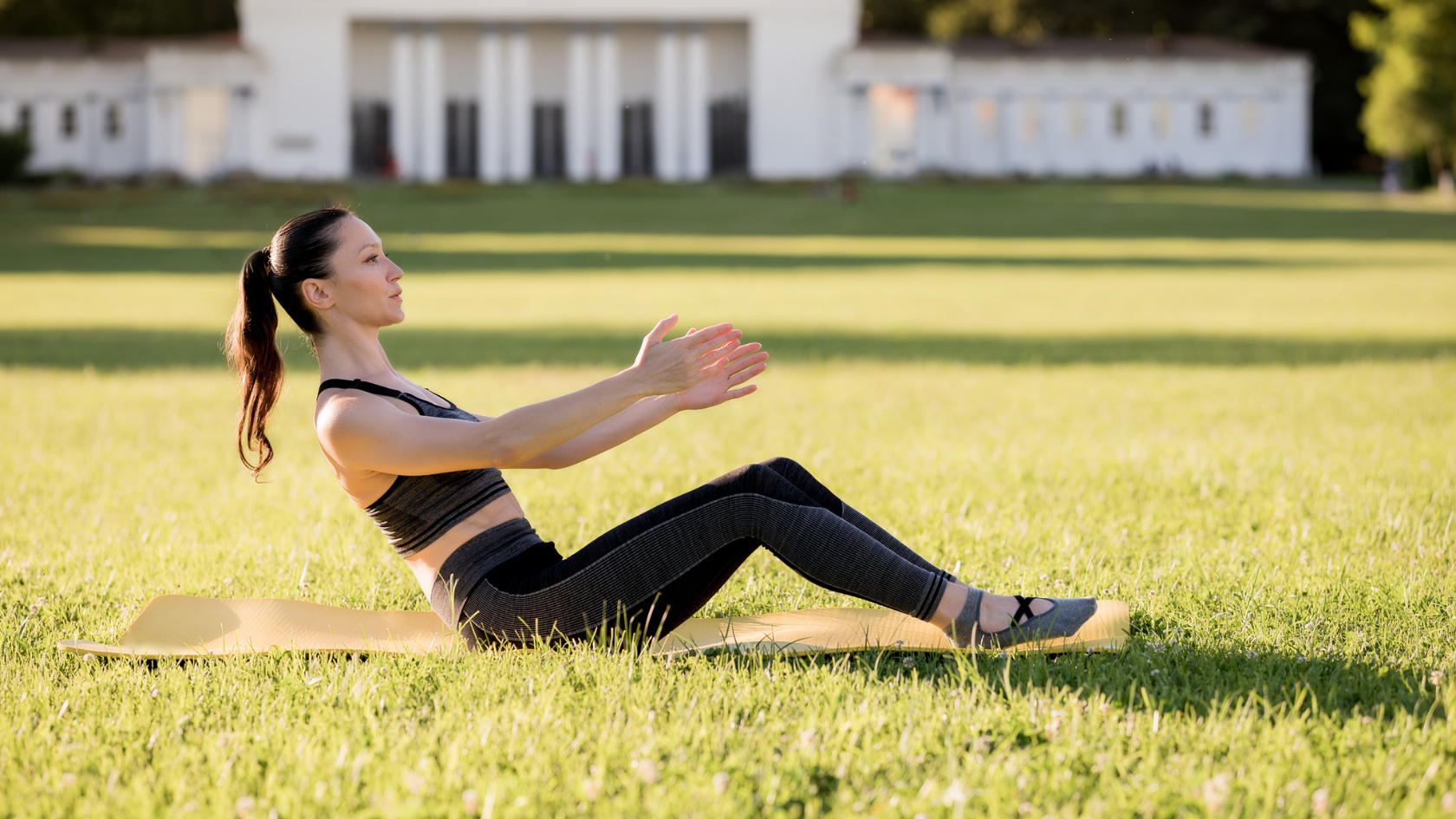 A woman doing a pilates rollup on a mat in the grass.