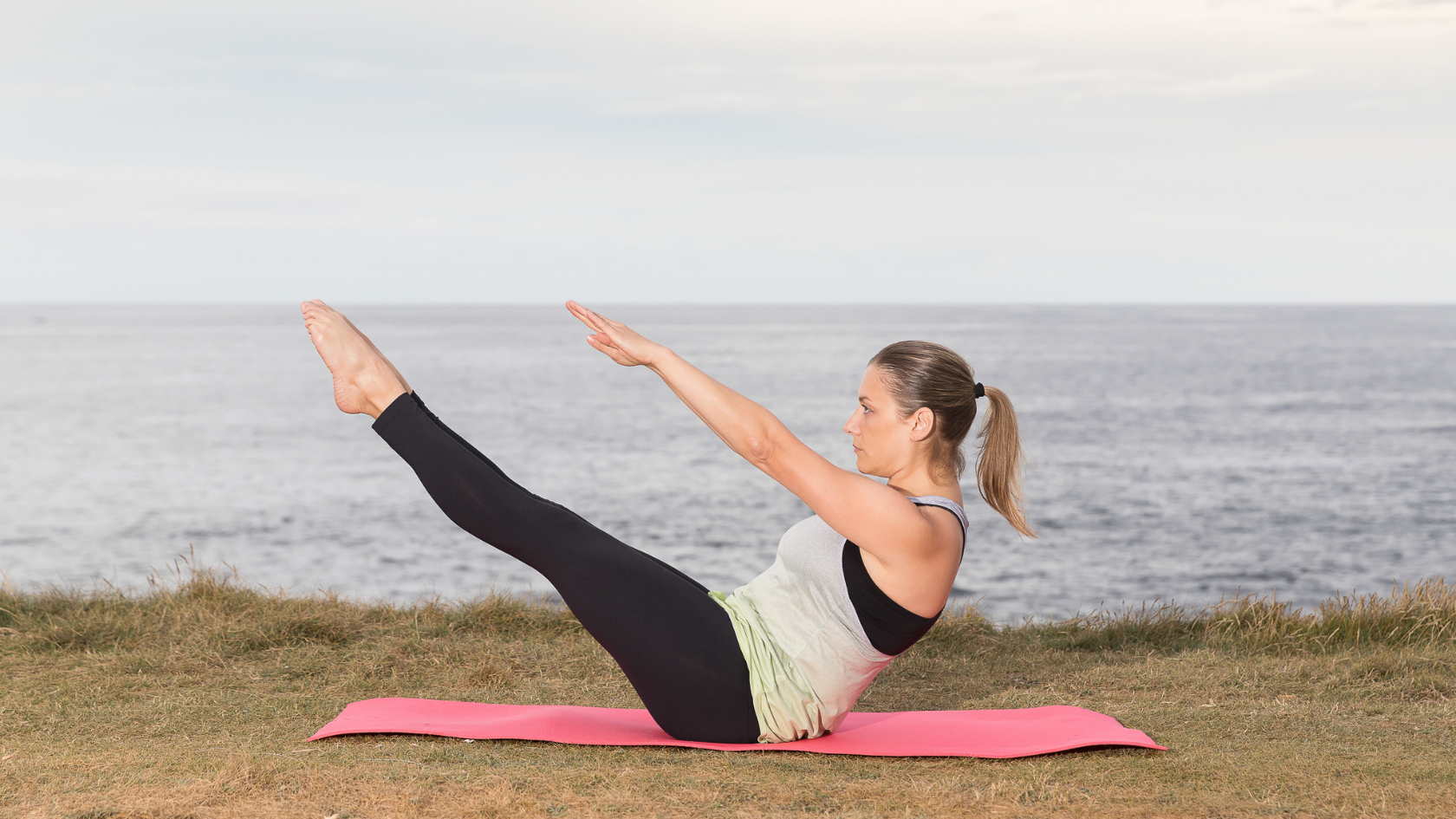 A woman doing yoga on a mat in front of the ocean.