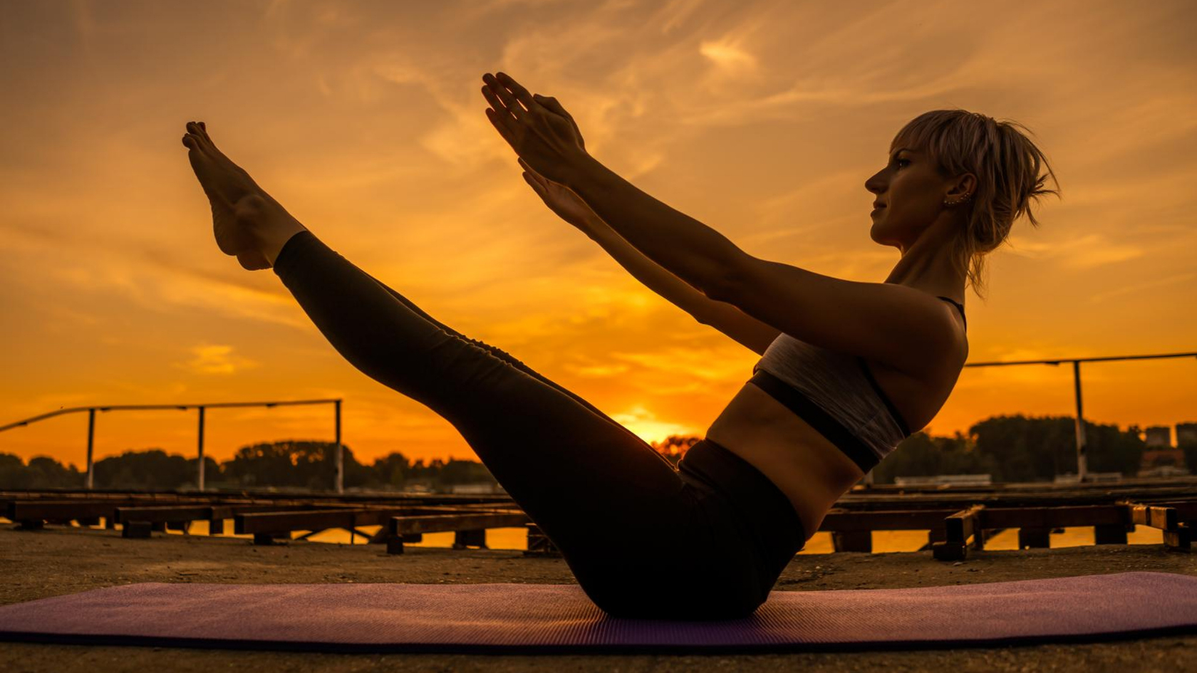 A woman doing a pilates teaser on a mat at sunset.