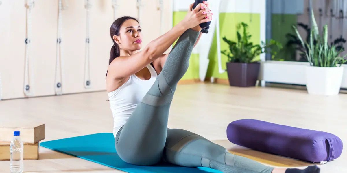 Woman performing a stretching exercise on a yoga mat in a fitness studio.