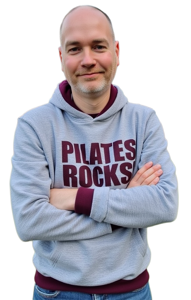 A man with short hair and a beard stands with arms crossed, wearing a gray hoodie that says "PILATES ROCKS" in bold letters.